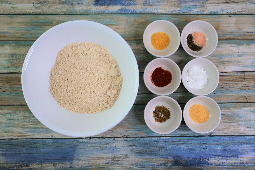 An overhead image of bowls containing Stone Ground 100% Whole Wheat Pastry Flour, garlic powder, smoked paprika, cayenne pepper, dried oregano, salt and pepper, baking powder and onion powder.