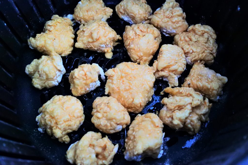 A close up overhead image of some popcorn chicken pieces being cooked in the basket of an air fryer