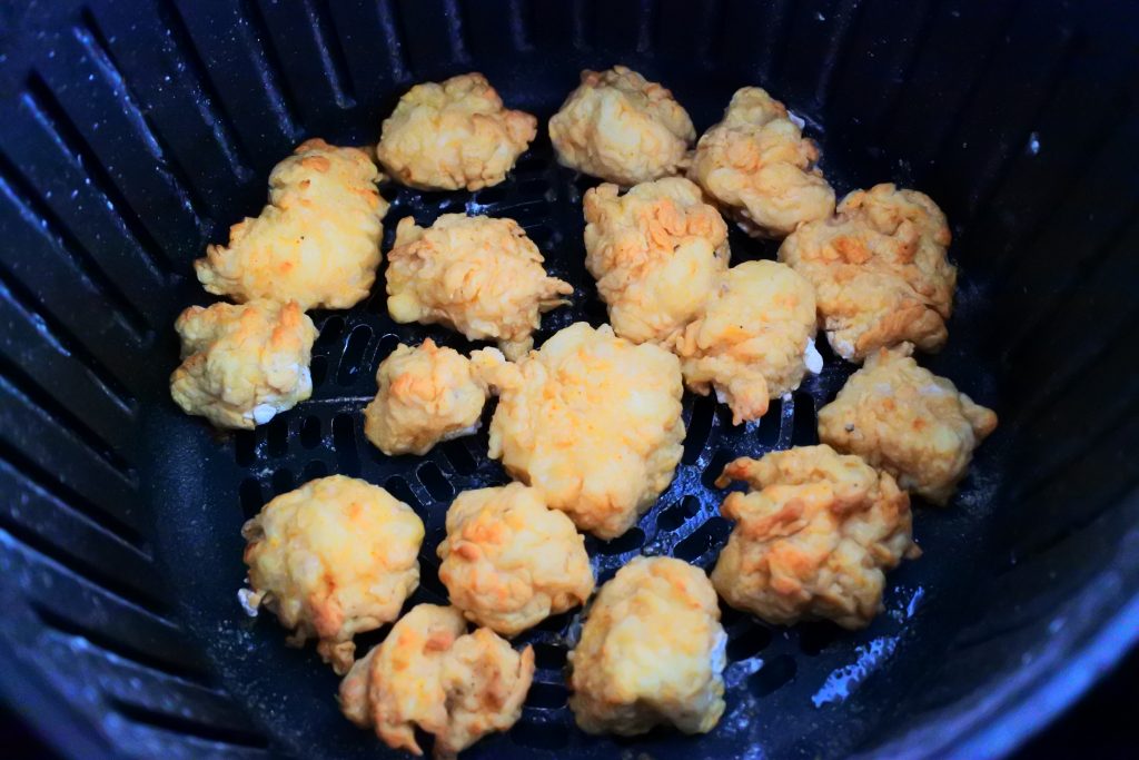 A close up overhead image of some popcorn chicken pieces in the basket of an air fryer