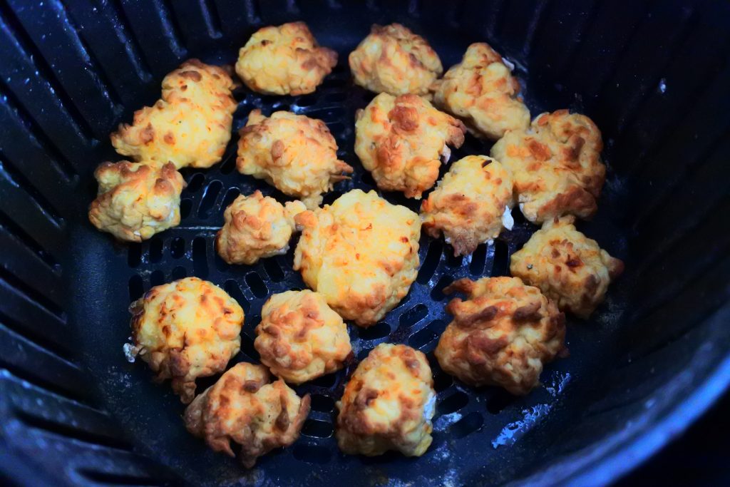 A close up overhead image of some browning popcorn chicken pieces in the basket of an air fryer