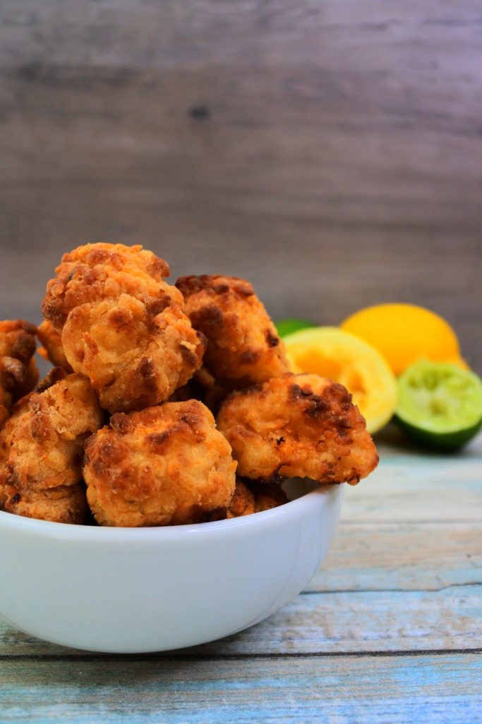 A vertical head on image of a bowl of popcorn chicken with some lemons and limes in the background