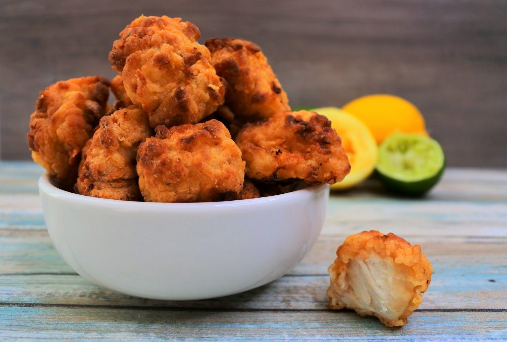 A close up image of a bowl of popcorn chicken with some lemons and limes in the background