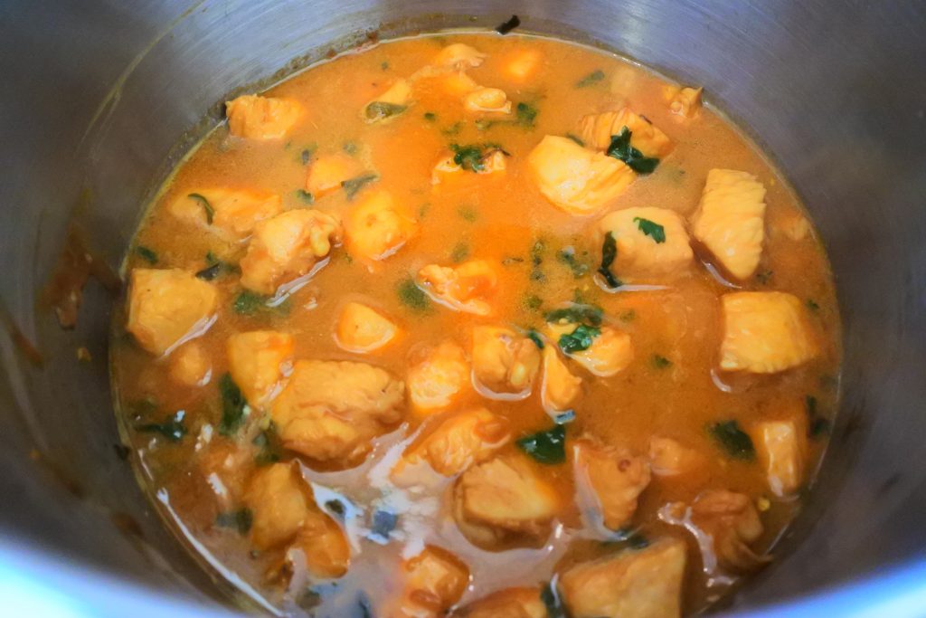 An angled image of Caribbean style stew chicken being cooked in a pot