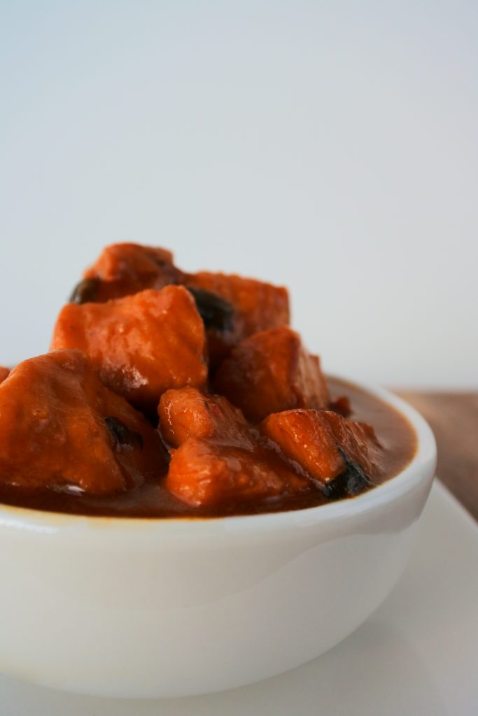 A head on image of a bowl of Caribbean-style stew chicken swimming in a rich caramelized gravy/sauce