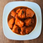 An overhead image of a bowl of Caribbean-style stew chicken swimming in a rich caramelized gravy/sauce