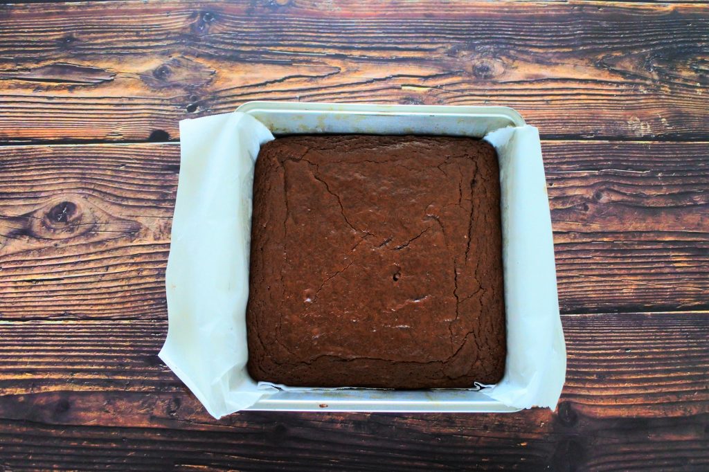 An overhead image of a square metal tin lined with parchment paper and filled with freshly baked, uncut brownies