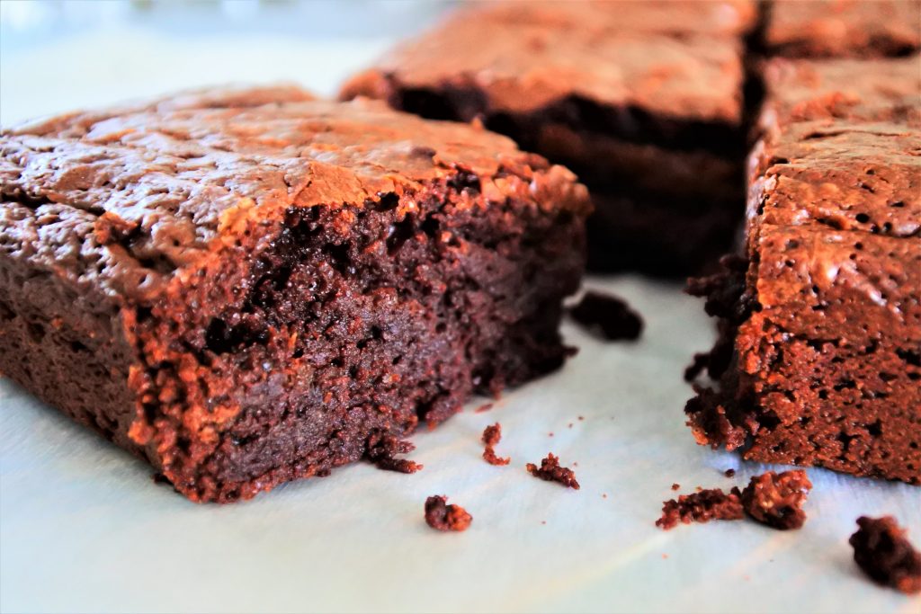 A close up image of a freshly cut square of brownie on a parchment sheet