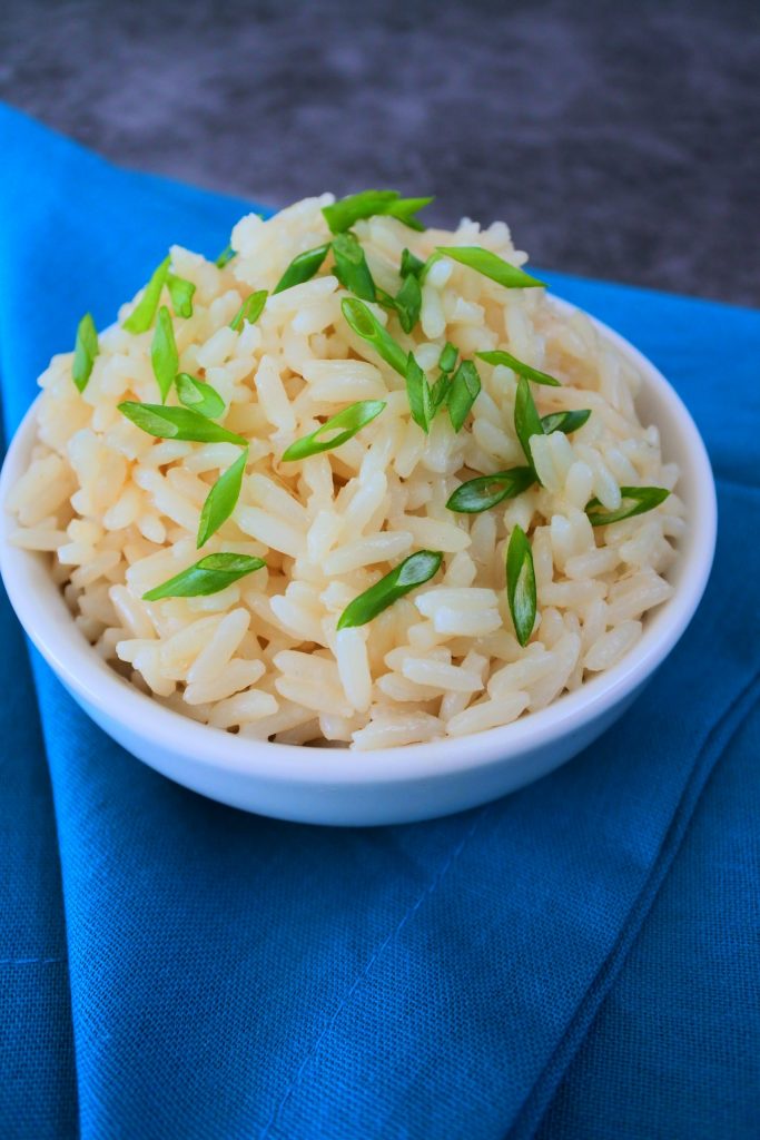 A head on image of a bowl of coconut infused rice topped with sliced chives on a blue linen napkin