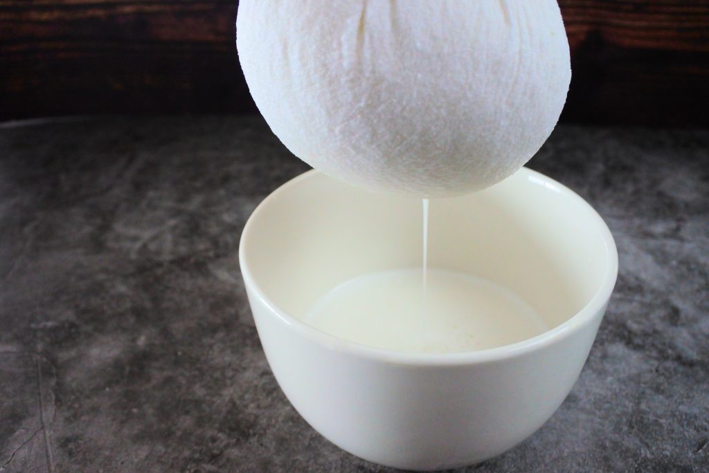 A head on image of coconut milk being strained out of a cheese cloth into a bowl