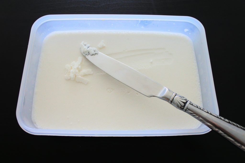 An overhead image of a container with separated coconut milk that's been chilled with a knife that's scraped the surface