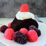 A head on image of a slice of chocolate cake with berries and coconut whipped cream