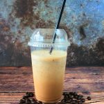 A head on image of a blended iced coffee frappe with a black straw surrounded by coffee beans.