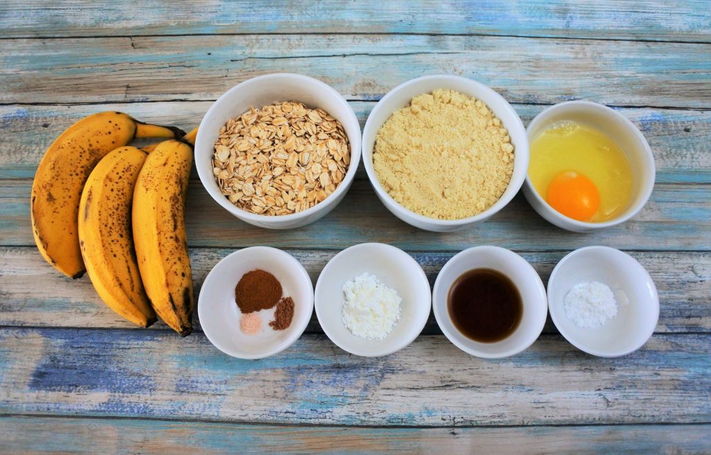 An overhead image of ingredients for banana oatmeal cookies including ripe bananas, rolled oats, almond flour, an egg, baking powder, vanilla, tapioca flour, and salt, nutmeg and cinnamon