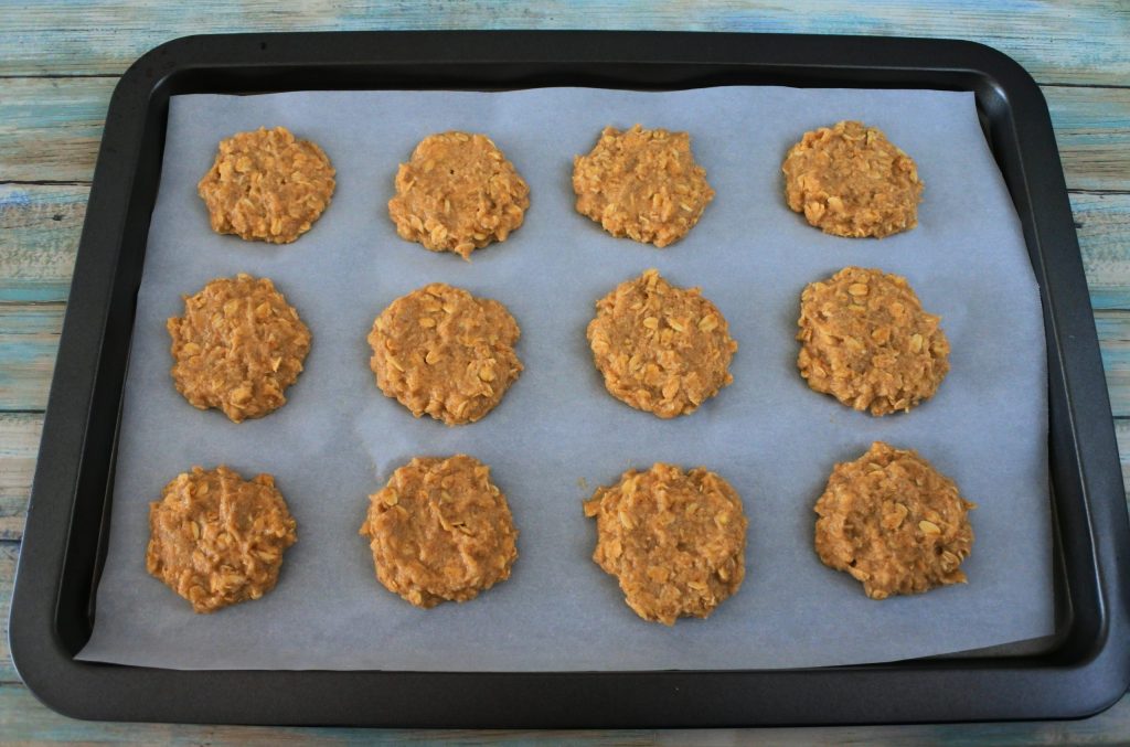 An angled image of a parchment-lined baking tray with unbaked banana oatmeal cookies on it