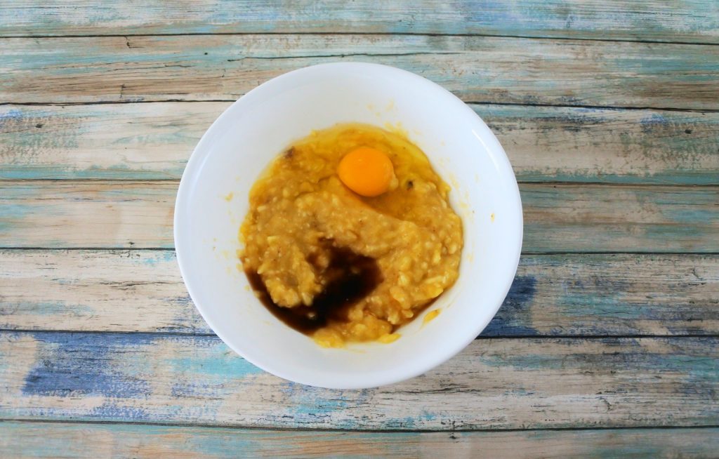 An overhead image of a bowl of mashed banana with an egg and vanilla extract added in