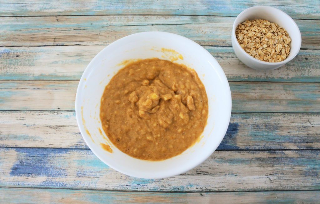 An overhead image of a bowl with a mashed banana and almond flour mixture with a smaller bowl containing rolled oats on the side