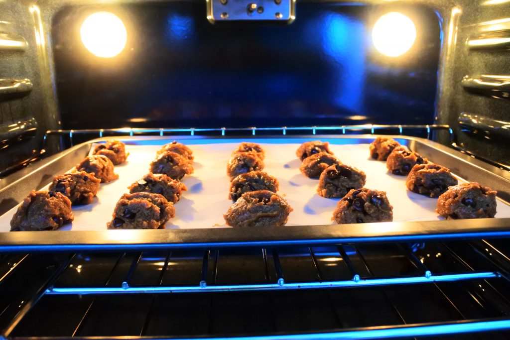 A head-on image of twenty portions of cookie dough on a tray in the oven