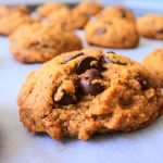 A head-on close up image of a chocolate chip cookie on a tray with a background of out-of-focus chocolate chip cookies