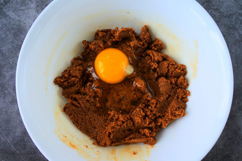 An overhead image of partially made peanut butter cookie dough with a cracked egg over it
