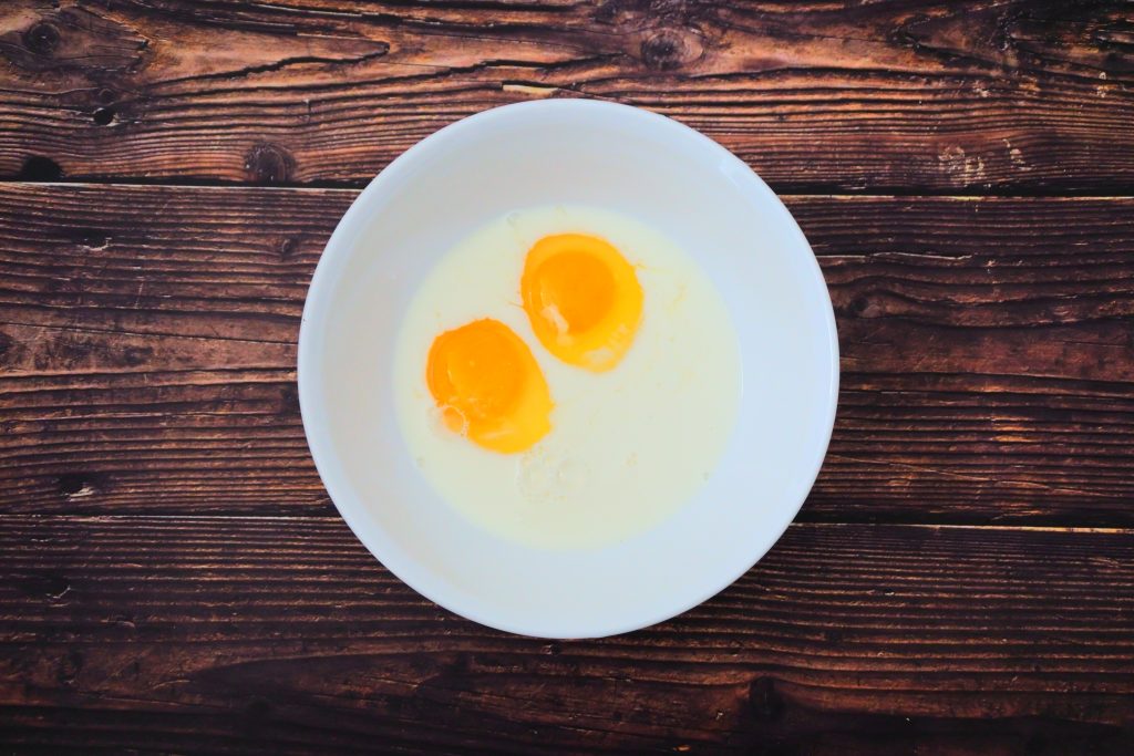 An overhead image of two cracked eggs in a bowl with some milk