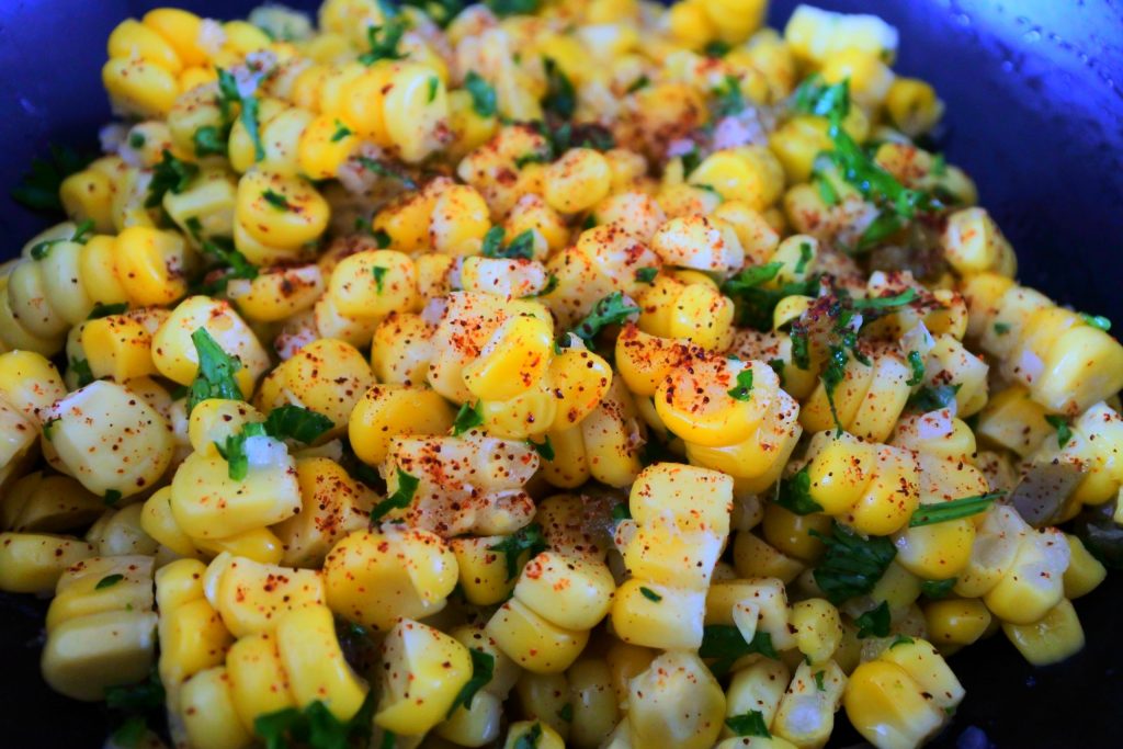 Close up image of corn tossed with spices and herbs for a corn salsa and topped with chili powder