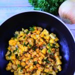 An overhead image of a bowl of corn salsa in a black bowl with fresh parsley lemon and an onion in the top corner