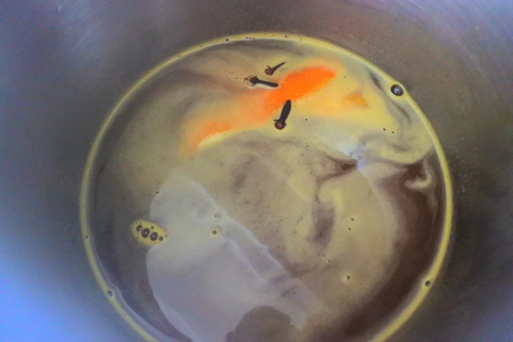 An overhead image of a pot with orange juice, with cloves and orange peel floating on the surface
