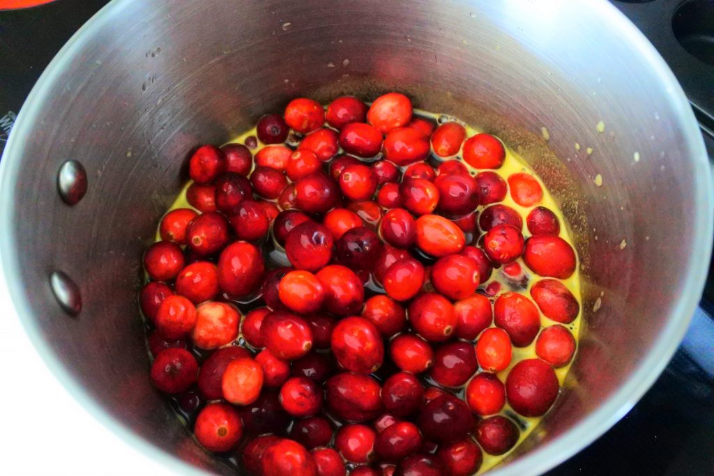 An angled overhead image of a pot with fresh cranberries in a spiced and sweetened orange juice