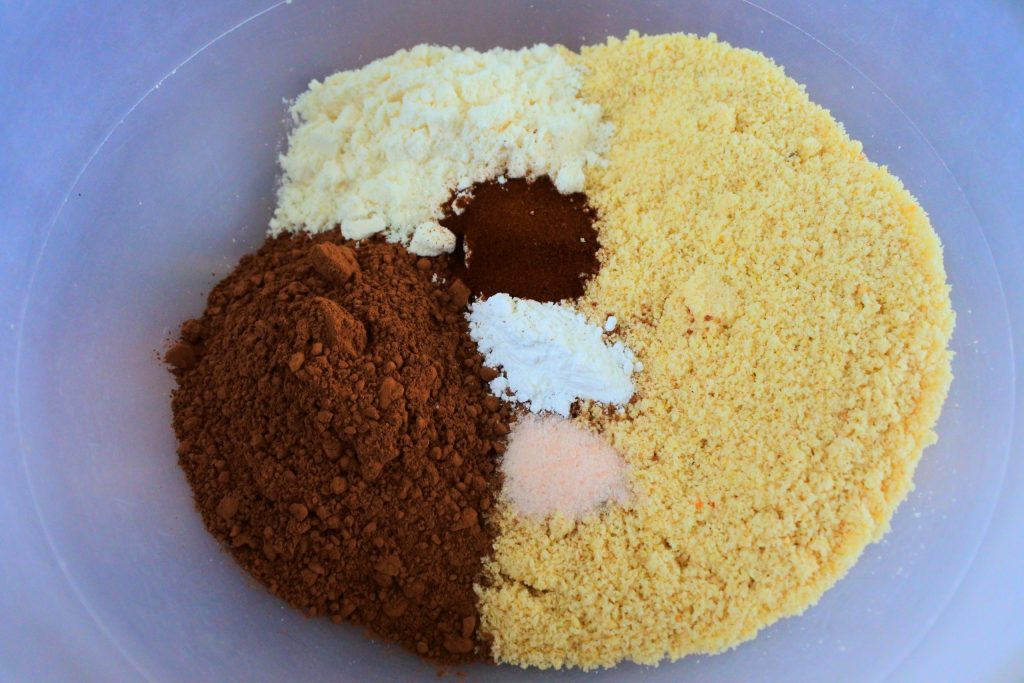 An overhead image of a bowl containing dry ingredients including almond flour, cocoa powder, coconut flour, espresso powder, baking powder and salt