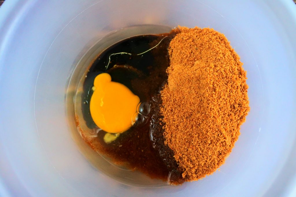 An overhead image of a bowl containing coconut sugar, an egg, molasses and oil