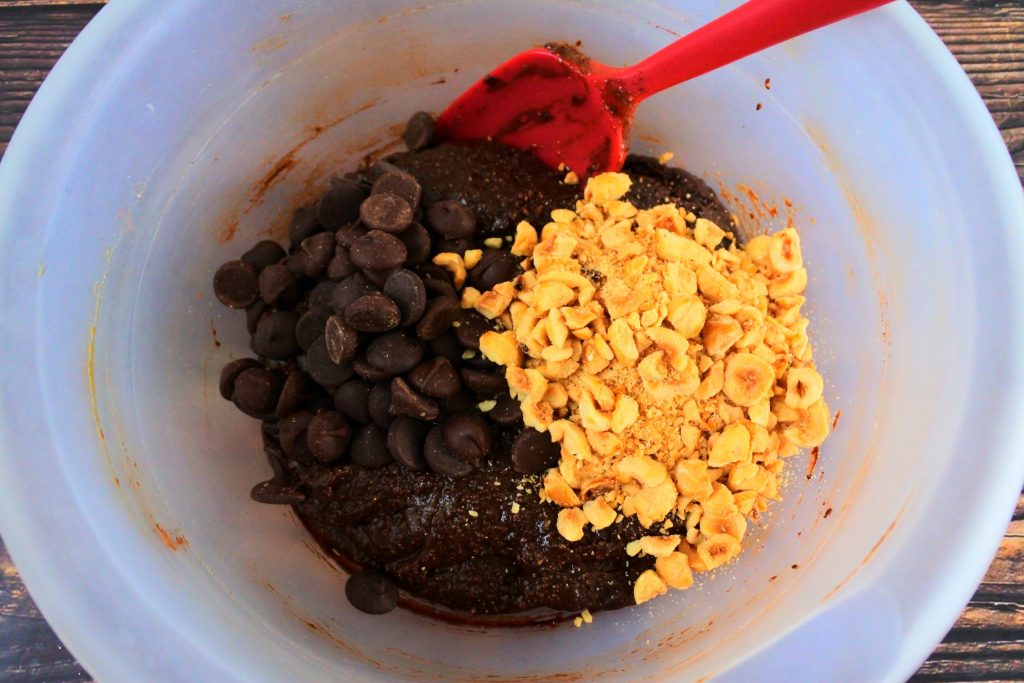 An overhead image of a bowl of chocolate cookie dough with chocolate chips and hazelnuts added in