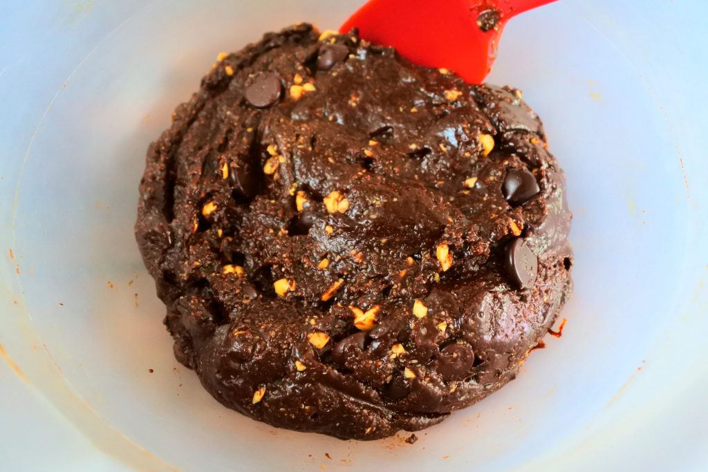 An overhead image of a bowl of chocolate cookie dough with chocolate chips and hazelnuts added in