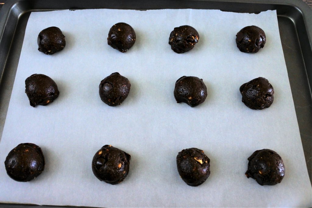 An angled image of a tray of domed tablespoon measures of Double Chocolate Hazelnut Cookie dough on a parchment lined baking tray