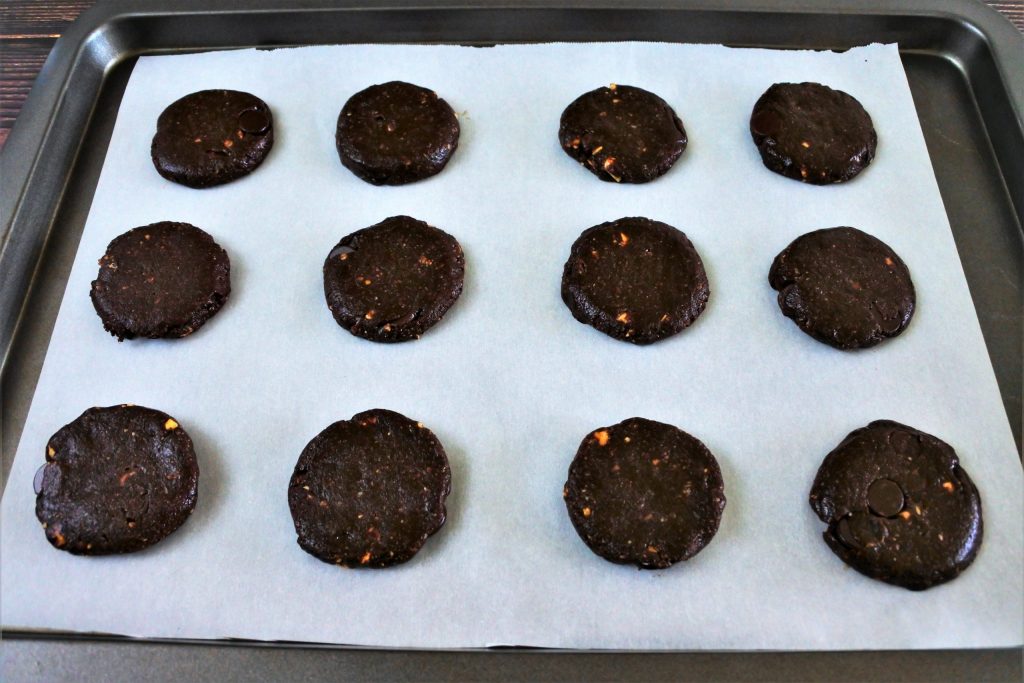 An angled image of a tray of flattened rounds of Double Chocolate Hazelnut Cookie dough on a parchment lined baking tray