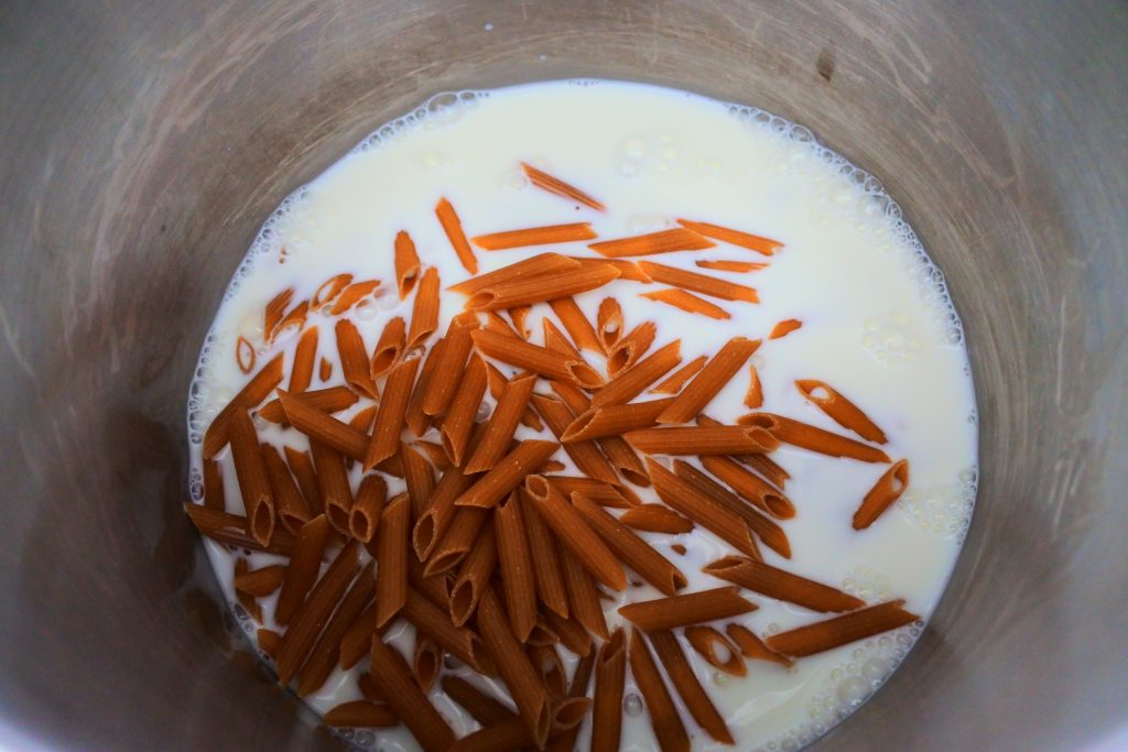 An overhead image of a pot with milk and whole grain penne pasta