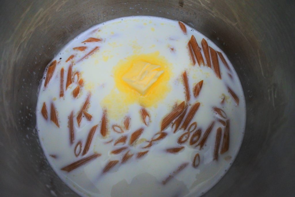 An overhead image of a pot of pasta being boiled in milk with a pat of butter