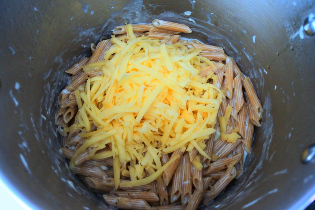 An overhead image of a pot of cooked penne pasta topped with shredded cheese