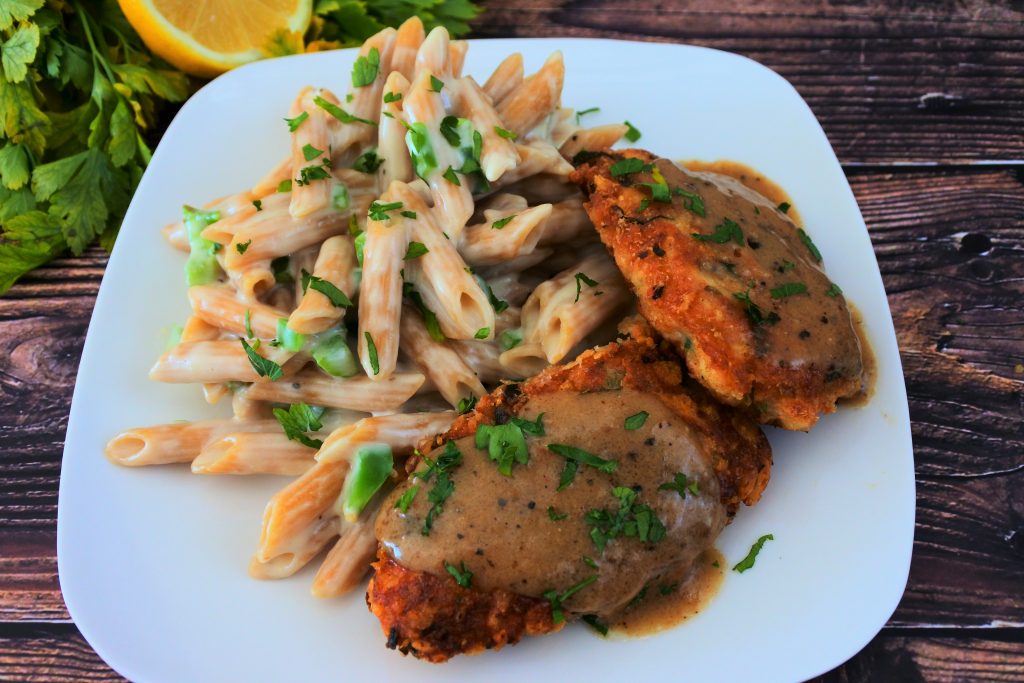 Am angled image of a plate of smoked gouda mac and cheese served with a Parmesan crusted chicken with some lemon and fresh herbs in the top left corner