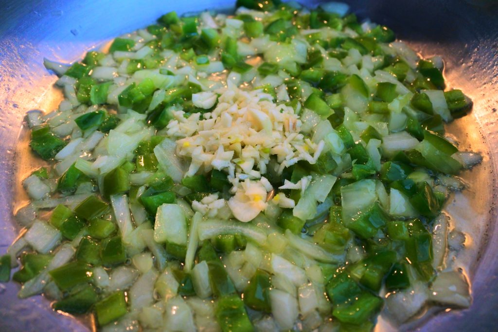 An angled head on image of a skillet with diced onions, garlic and bell peppers