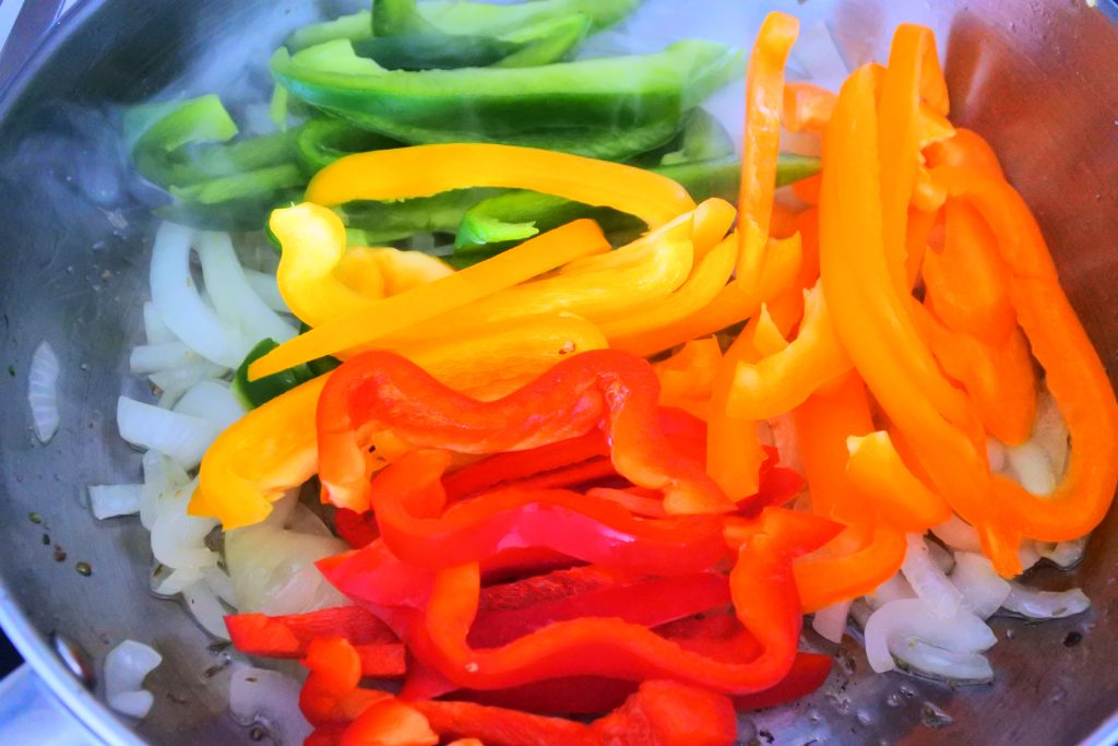 An overhead image of multicolored bell peppers on top of onions in a pan