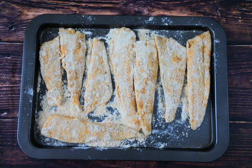 An overhead image of a tray of floured fish fillets.