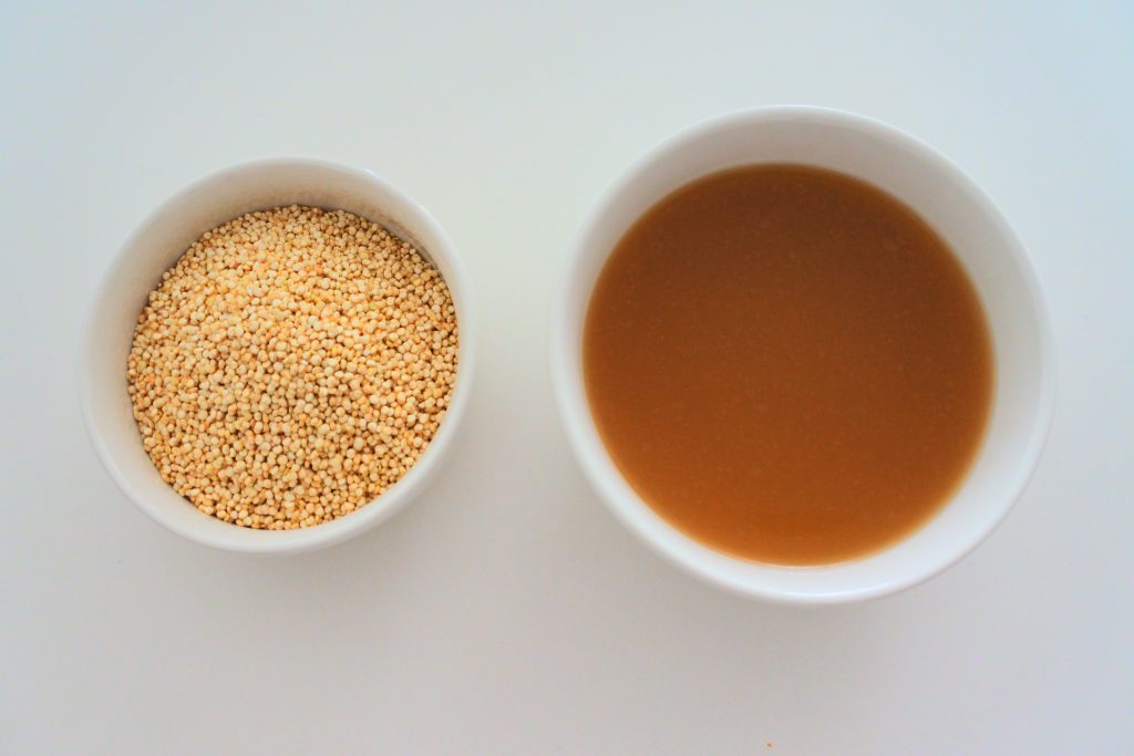 An overhead image of a bowl of uncooked quinoa next to a bowl of broth