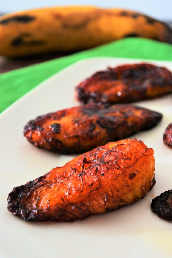 A close up image of slices of fried plantains with a whole plantain in the background