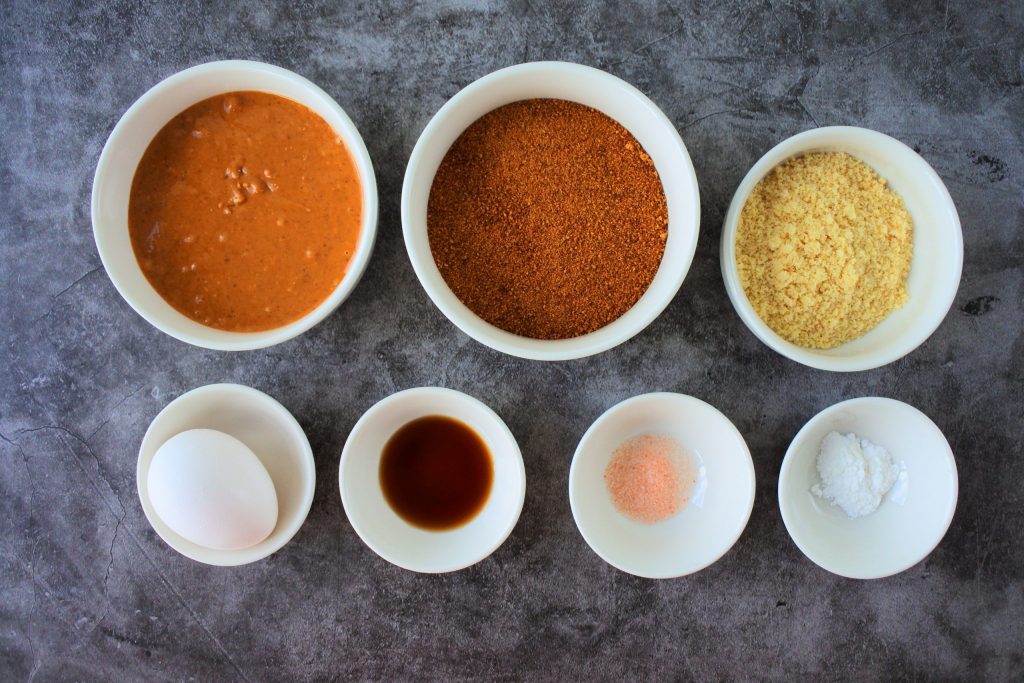An overhead image of bowls of ingredients for a gluten free peanut butter cookie including: natural peanut butter, coconut sugar, almond flour, an egg, vanilla extract, salt, and baking powder