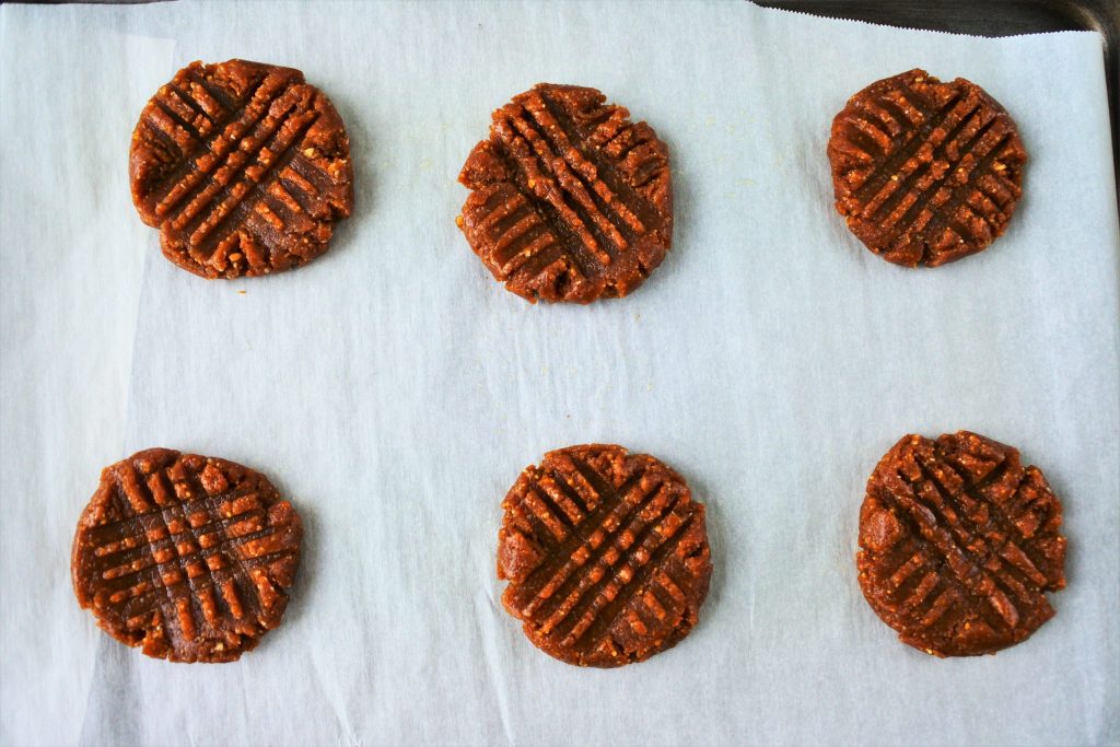 An overhead image of unbaked, pressed peanut butter cookies on a parchment paper lined tray