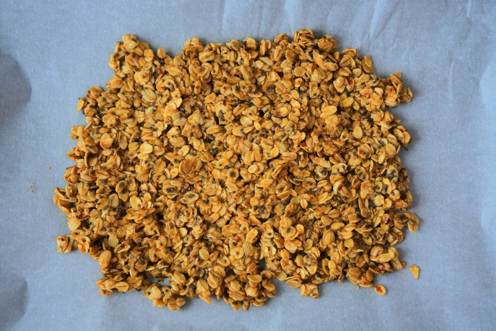 An overhead image of baked granola on a sheet of parchment paper