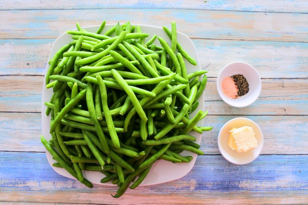 An overhead image of a plate of green beans next to small dishes of butter and salt and pepper.