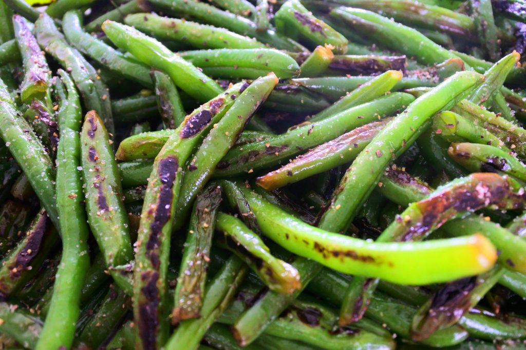A close up image of blistered green beans seasoned with salt and pepper