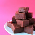 A head on image of a plate of homemade chocolate fudge pieces against a pink background