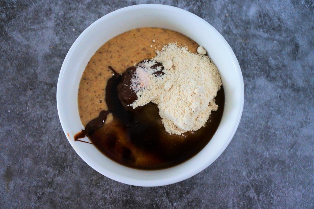 An overhead image of a bowl of hazelnut butter with melted dark chocolate, vanilla extract, finely ground sugar, and a pinch of salt